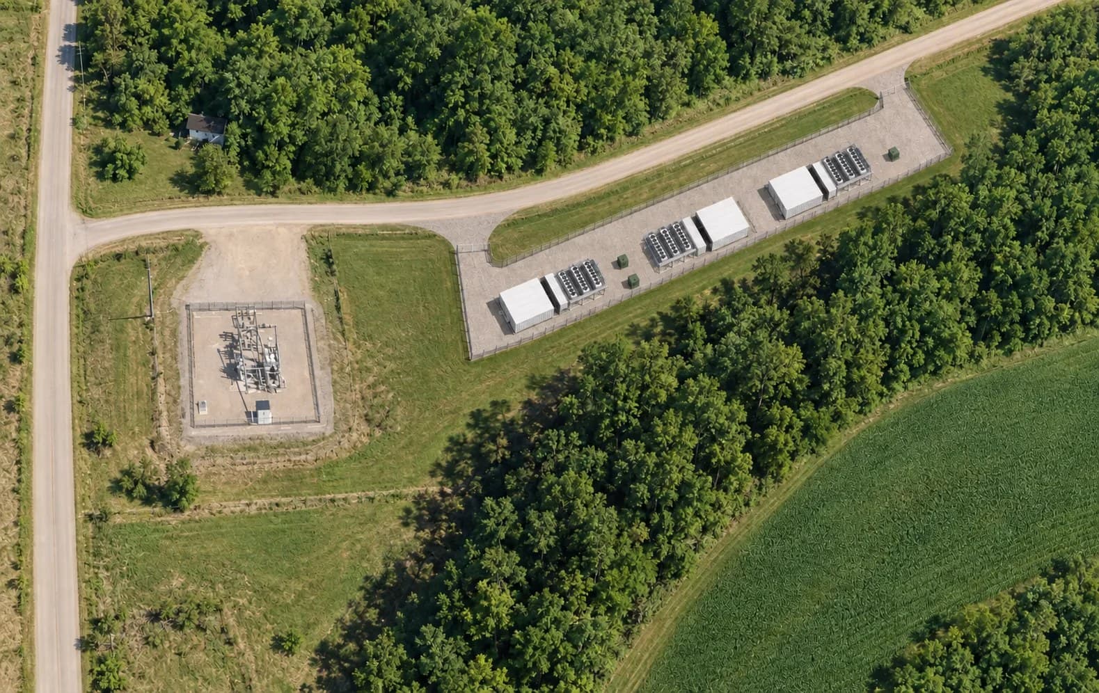 Conceptual aerial rendering of the proposed Plymouth site: a single row of low modular compute units with cooling units beside them on a fenced gravel pad along the road, next to the existing Oakdale Electric substation, surrounded by woods and farm fields